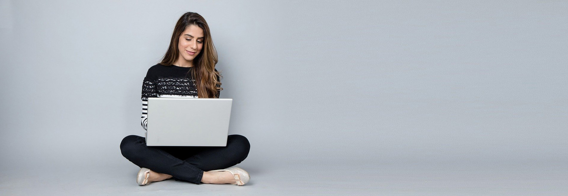 Frau mit Laptop im Schneidersitz vor grauer Wand